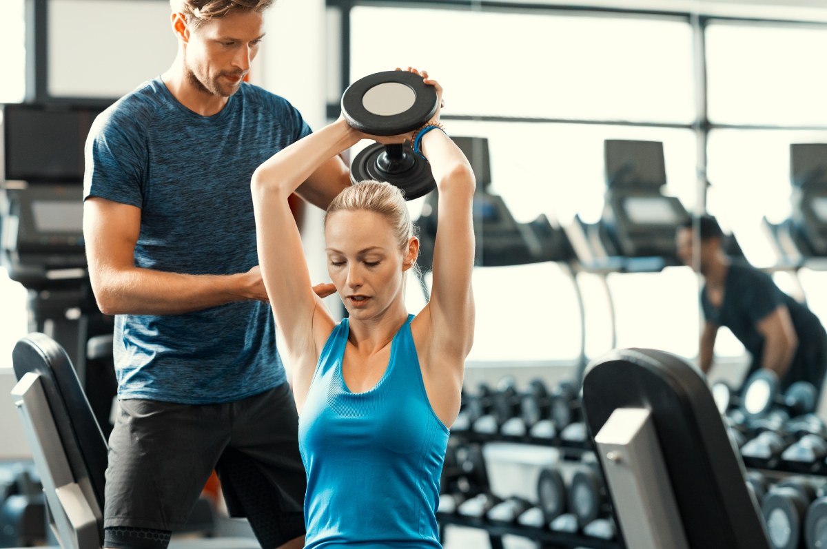 Personal trainer giving weightlifting training to girl in gym.