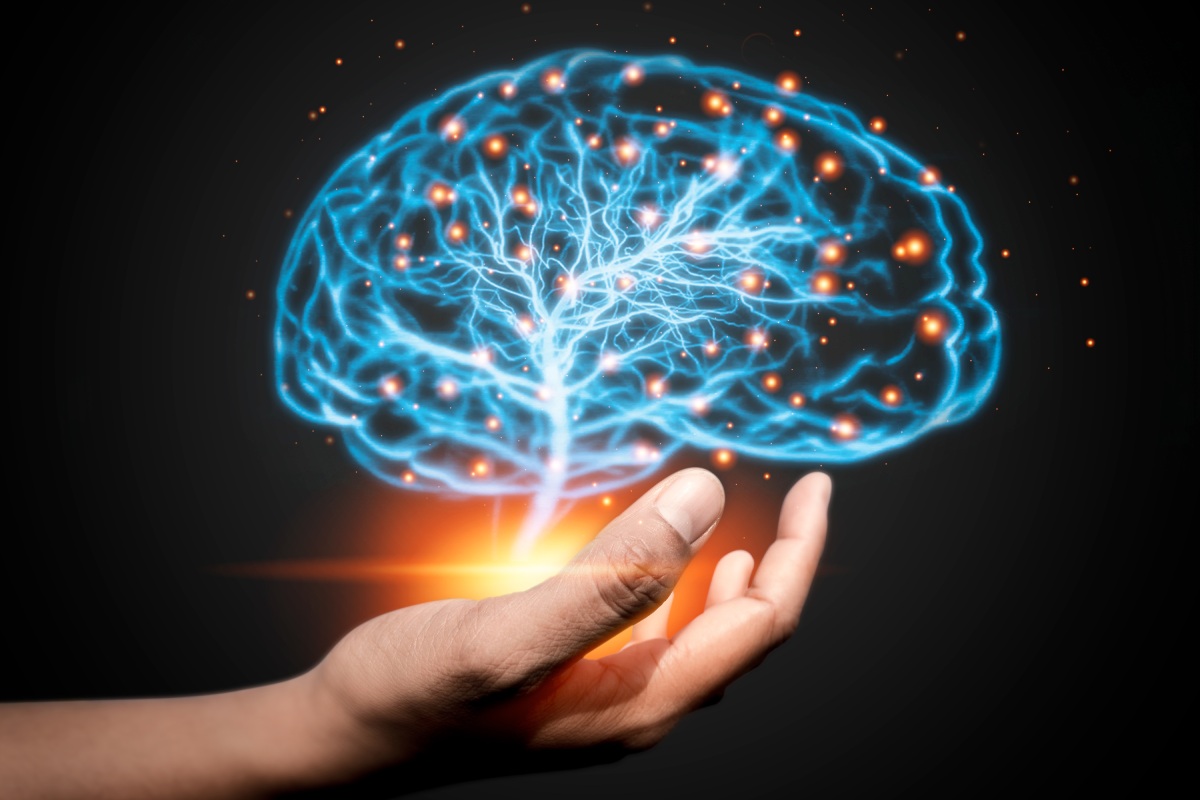 A hand holding a digital representation of a human brain with glowing network connections against a dark background.