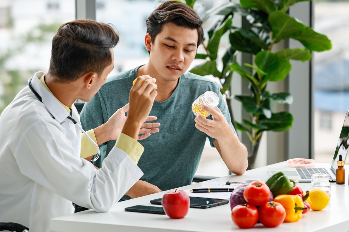 Male nutritionist showing and discussing vitamin pills with Asian man .