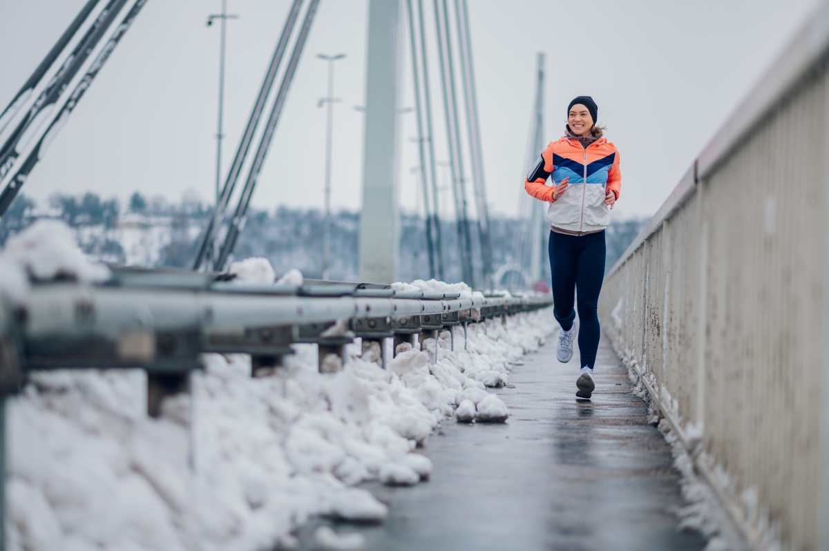 Smiling female runner jogging on a bridge during winter.