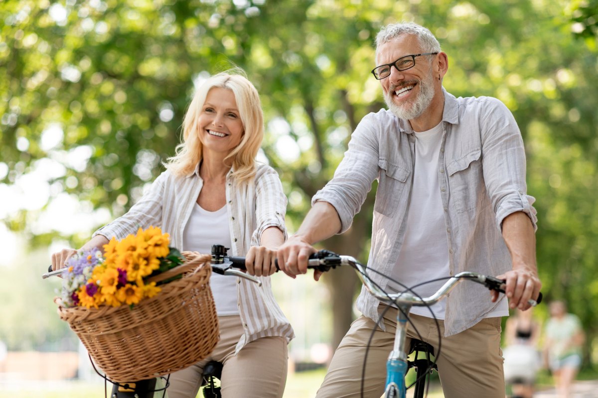 Happy Mature Couple Riding Retro Bicycles In Summer Park