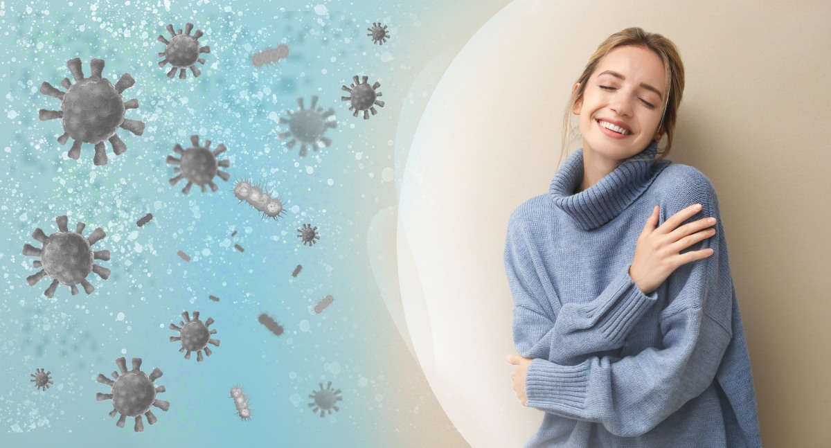 A woman in a blue sweater smiles and hugs herself while standing against a light background. Virus icons are depicted on the left side of the image.