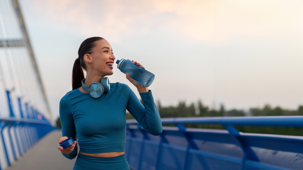 woman relaxing and drinking water on seaside promenade after running