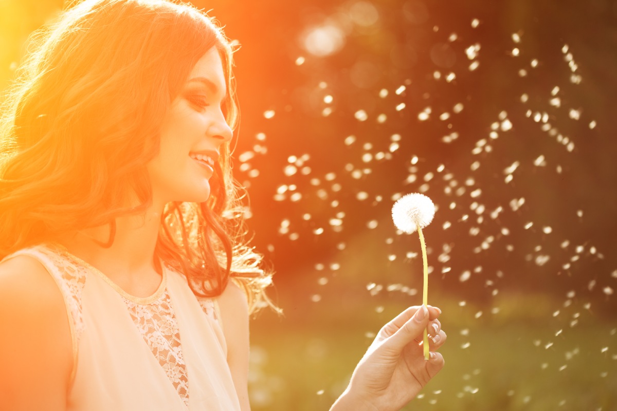 Woman blowing dandelion seeds in the sunlight.