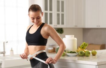 Weight loss. Woman measuring waist with tape in kitchen